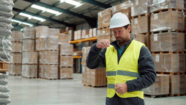 Video of male warehouse worker standing in warehouse. Warehouse employee putting on a working helmet.