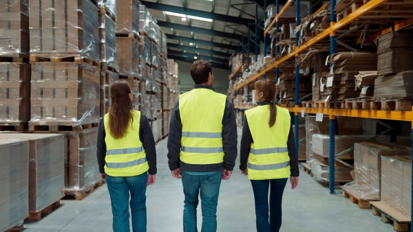 Rear view of warehouse workers in reflective vest walking in warehouse. Team of warehouse workers preparing products for shipment.