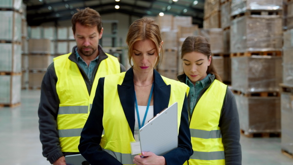 Team of warehouse employees standing in warehouse. Team of workers in reflective clothing in modern industrial factory, heavy industry, manufactrury. Group video.