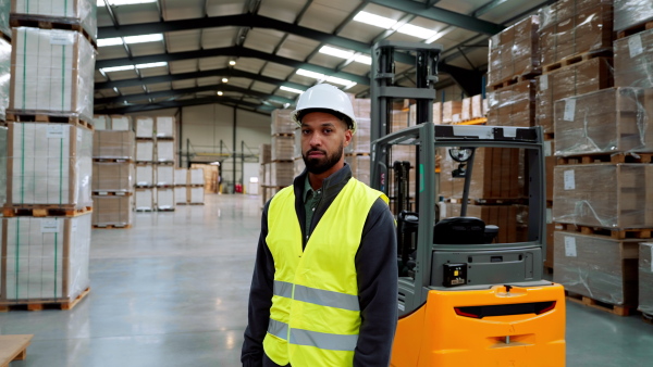 Video of male warehouse worker standing by forklift. Warehouse manager checking delivery, stock in warehouse, inspecting products for shipment.