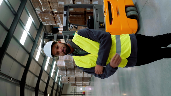 Video of male warehouse worker standing by forklift. Warehouse manager checking delivery, stock in warehouse, inspecting products for shipment. Vertical view.