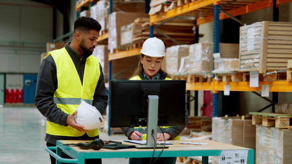 Warehouse manager talking with logistics employee in warehouse, planning transport of products, goods, talking shipping process.