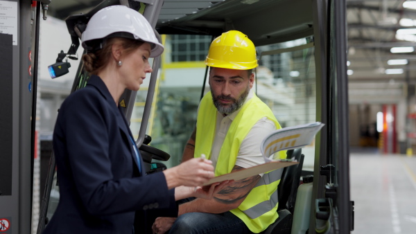 A warehouse manager checking delivery, stock in warehouse, inspecting forklift driver.