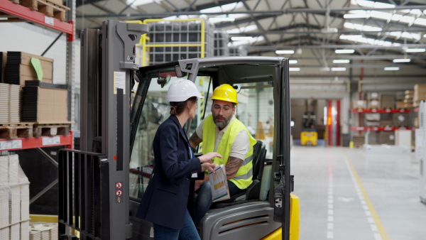 A warehouse manager checking delivery, stock in warehouse, inspecting forklift driver.