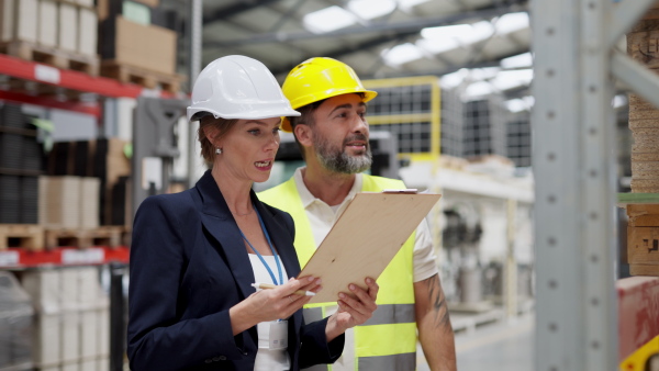 Female warehouse director talking with production manager, discussing new order, preparing products for shipmennt, delivery, checking stock in the warehouse.