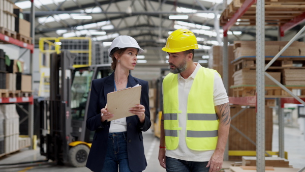 Female warehouse director talking with production manager, discussing new order, preparing products for shipmennt, delivery, checking stock in the warehouse.