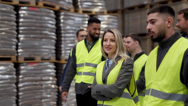 Full team of warehouse employees walking in warehouse. Team of workers, managers and female director in modern industrial factory, heavy industry, manufactrury. Group portrait.