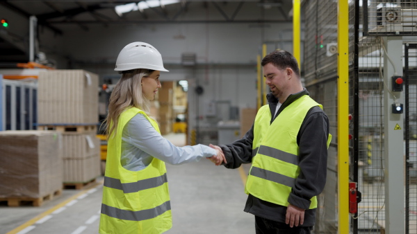 A young man with Down syndrome working in warehouse, colleague shaking hands with him. Concept of workers with disabilities, support in workplace.