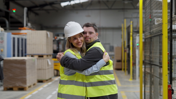 Young man with Down syndrome working in warehouse, colleague talking with him. Concept of the workers with disabilities, support in workplace.