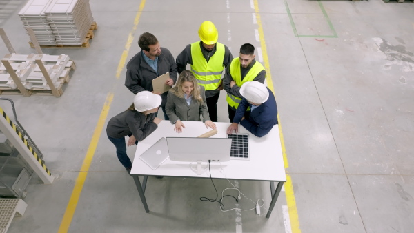 A top view of team of engineers and foremans consulting with director in modern industrial factory, talking about new production project or investment. Team management in manufacturing facility.