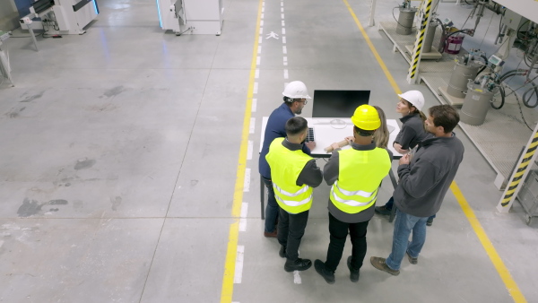 A top view of team of engineers and foremans consulting with director in modern industrial factory, talking about new production project or investment. Team management in manufacturing facility.