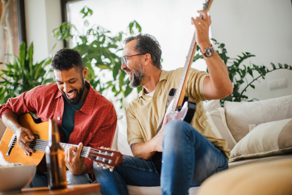 Best friends, musician jamming together. Playing music on acoustic and electric guitar together, having beer and fun. Concept of male friendship, bromance.