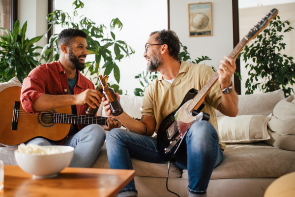 Best friends, musician jamming together. Playing music on acoustic and electric guitar together, having beer and fun. Concept of male friendship, bromance.