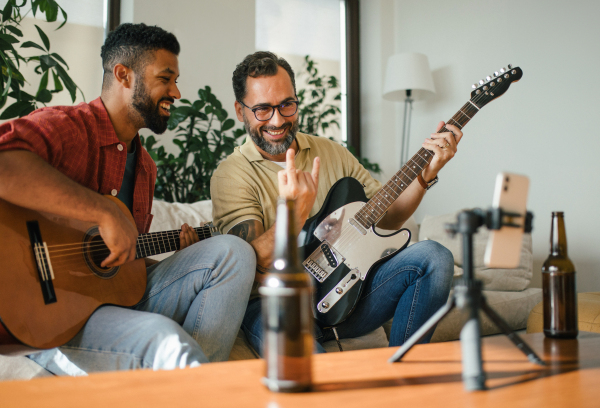 Best friends, musician jamming together, making video on social media. Playing music on acoustic and electric guitar together at home for fans. Concept of male friendship, bromance.