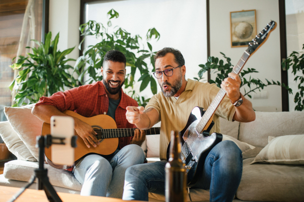 Best friends, musician jamming together, making video on social media. Playing music on acoustic and electric guitar together at home for fans. Concept of male friendship, bromance.