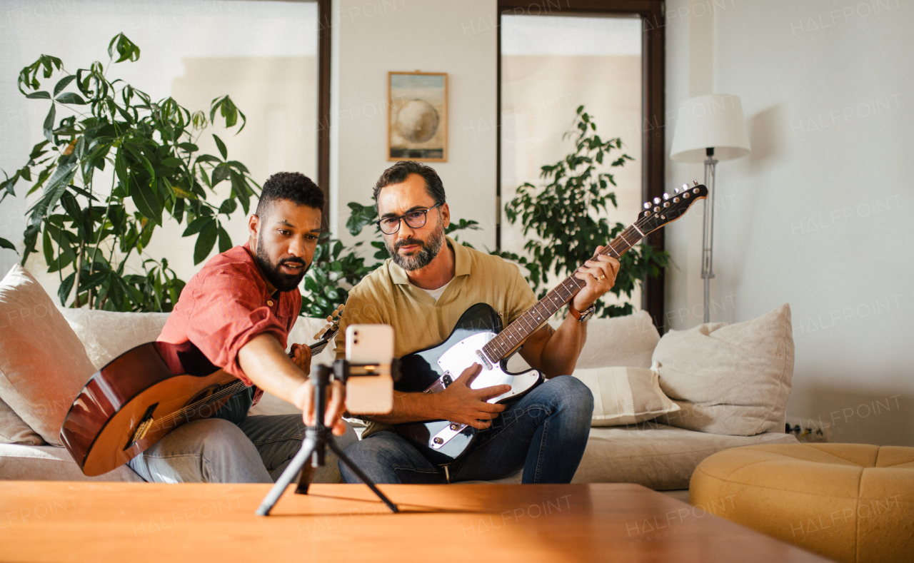 Best friends, musician jamming together, making video on social media. Playing music on acoustic and electric guitar together at home for fans. Concept of male friendship, bromance.