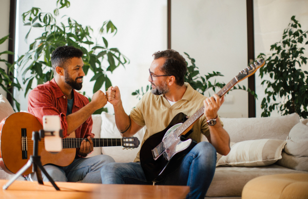 Best friends, musician jamming together, making video on social media. Playing music on acoustic and electric guitar together at home for fans. Concept of male friendship, bromance.