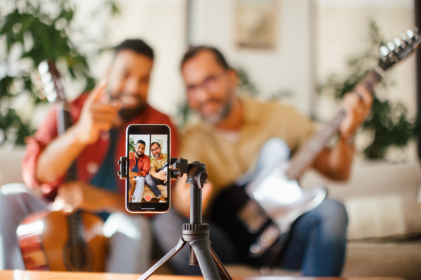 Best friends, musician jamming together, making video on social media. Playing music on acoustic and electric guitar together at home for fans. Concept of male friendship, bromance.