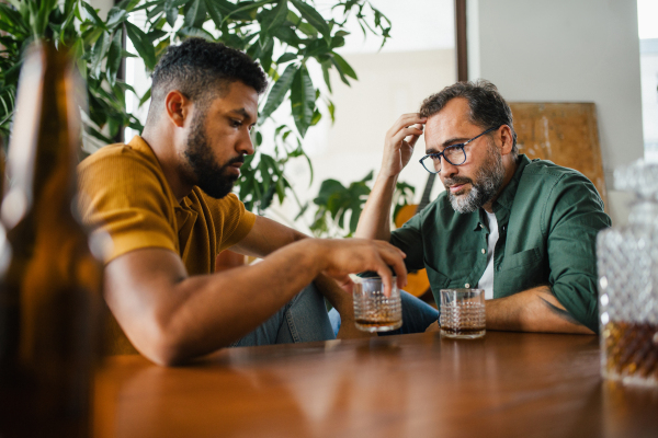 Best friends, supporting each other, drinking whiskey and talking. Discussing problems and drowning sorrows in alcohol. Concept of male friendship and bromance.