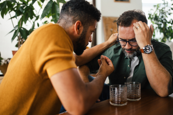 Best friends, supporting each other, drinking whiskey and talking. Discussing problems and drowning sorrows in alcohol. Concept of male friendship and bromance.