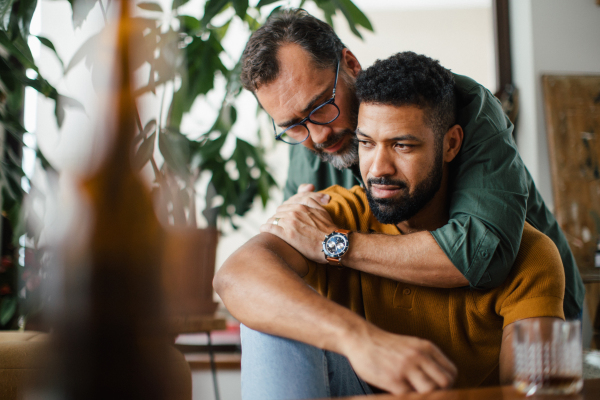 Man hugging best friend, supporting each other, drinking whiskey and talking. Discussing problems and drowning sorrows in alcohol. Concept of male friendship and bromance.