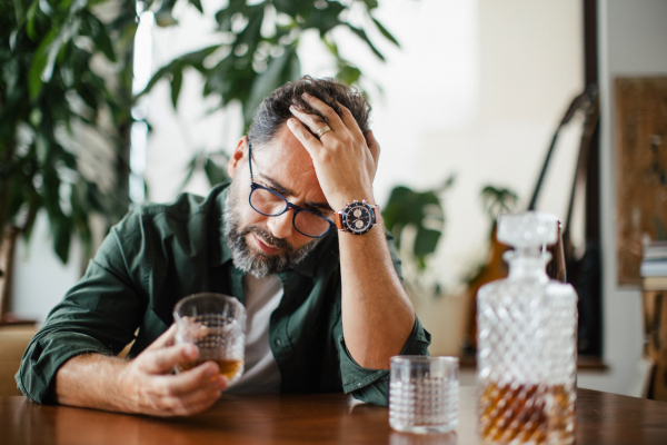 Sad man drinking whiskey and thinking. Having problems, drowning sorrows in the alcohol.