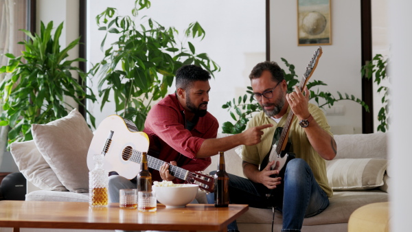 Best friends, musician jamming together. Playing music on acoustic and electric guitar together, having beer and fun. Concept of male friendship, bromance.