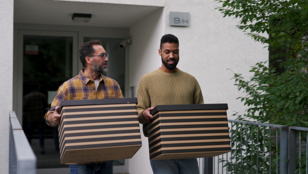 Man helping his friend move into new apartment in building. Man is moving into new flat, carrying box from the moving truck and phone calling.