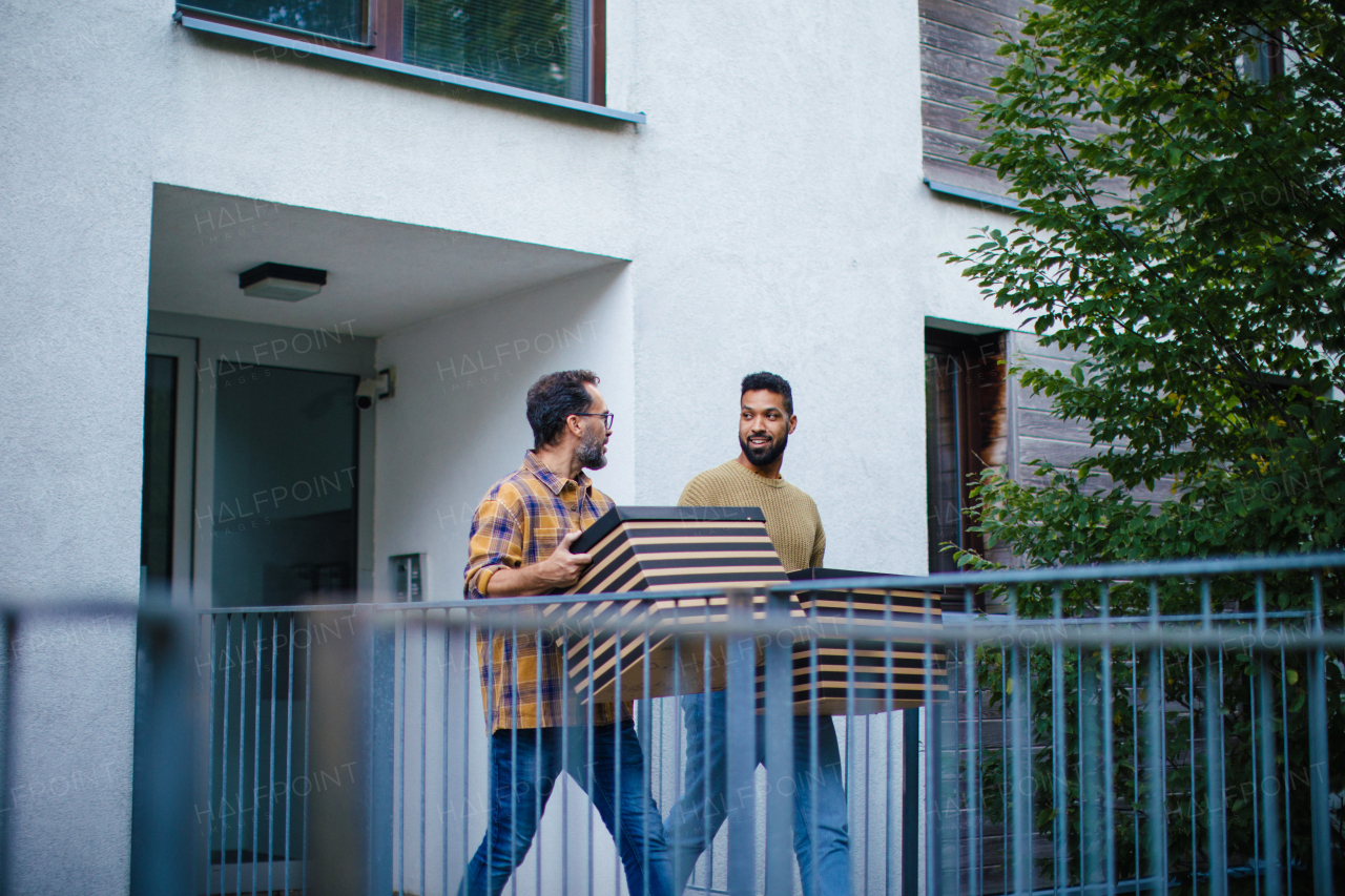 Man helping his friend move into new apartment in building. Man is moving into new flat, carrying box from the moving truck and talking.