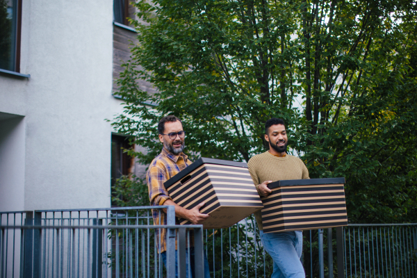 Man helping his friend move into new apartment in building. Man is moving into new flat, carrying box from the moving truck and talking.