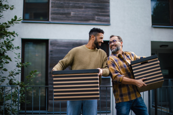 Man helping his friend move into new apartment in building. Man is moving into new flat, carrying box from the moving truck and talking.