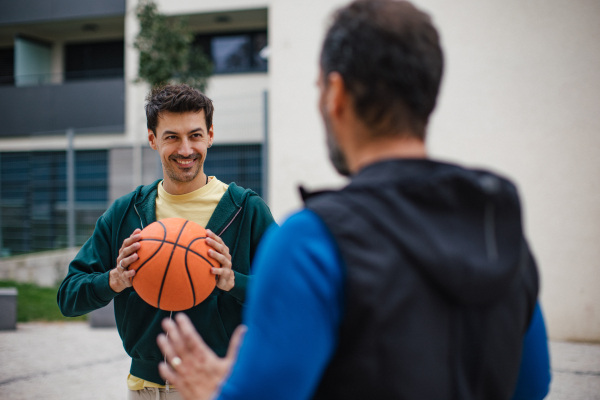 Best friends playing sport outdoors, having fun, competing. Playing basketball at local court, enjoying exercise together. Concept of male friendship, bromance.