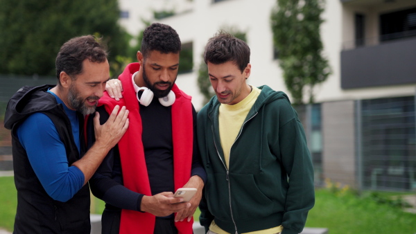 Best friends playing sport outdoors, having fun, competing. Watching content on smartphone. Concept of male friendship, bromance.