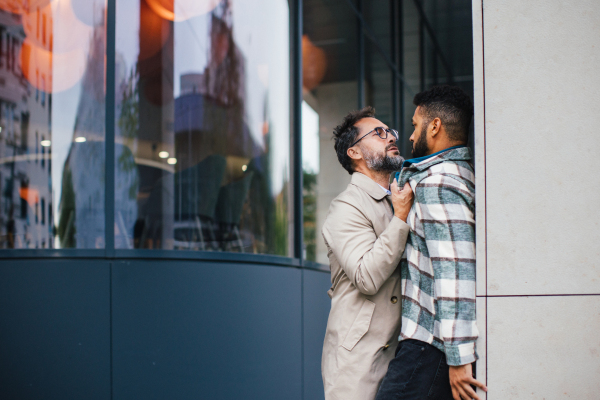 Violence against man on street, racist attack. Angry man is aggressive, have conflict with young man, holding him by shirt, screaming, threatening him.