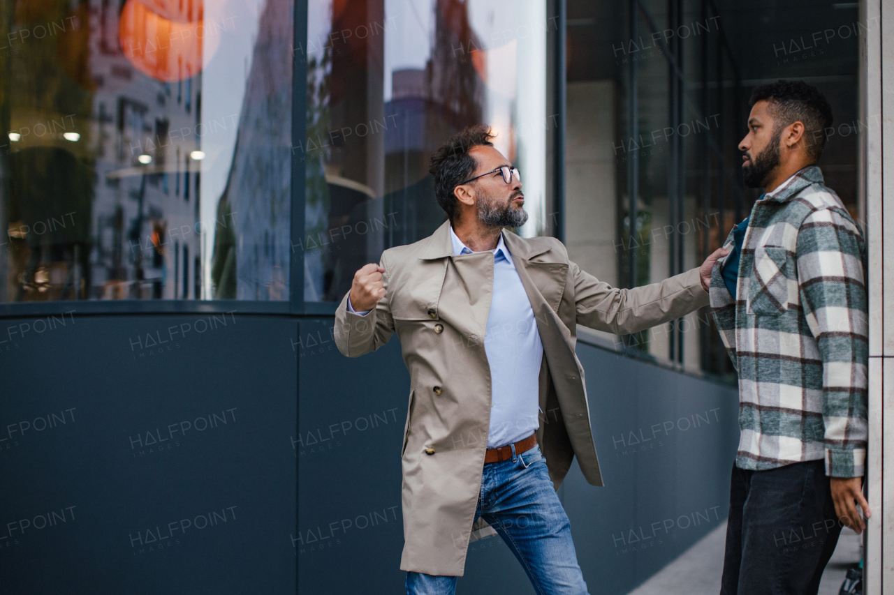 Violence against man on street, racist attack. Angry man is aggressive, have conflict with young man, holding him by shirt, screaming, threatening him.