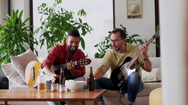 Best friends, musician jamming together. Playing music on acoustic and electric guitar together, having beer and fun. Concept of male friendship, bromance.