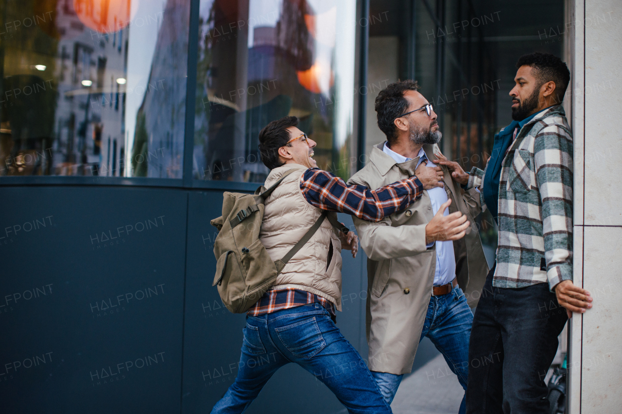 Angry man is aggressive, have conflict with young man, holding him by shirt, screaming, threatening him. Friend helping to end fight, attack.