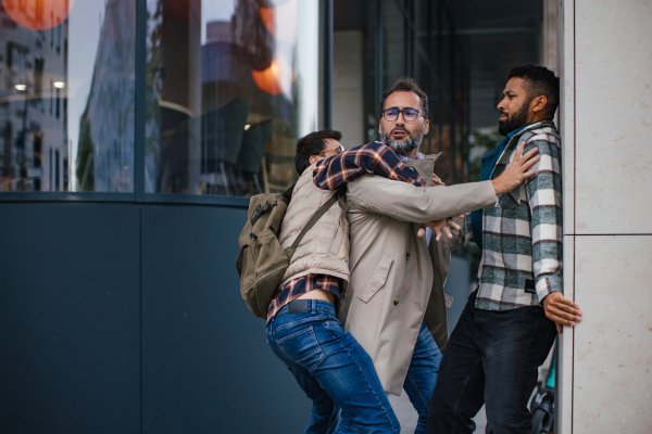 Angry man is aggressive, have conflict with young man, holding him by shirt, screaming, threatening him. Friend helping to end fight, attack.