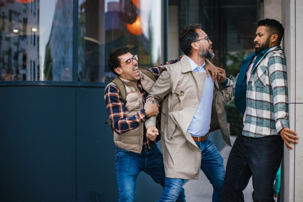 Angry man is aggressive, have conflict with young man, holding him by shirt, screaming, threatening him. Friend helping to end fight, attack.