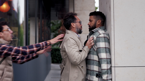 Angry man is aggressive, have conflict with young man, holding him by shirt, screaming, threatening him. Friend helping to end fight, attack.