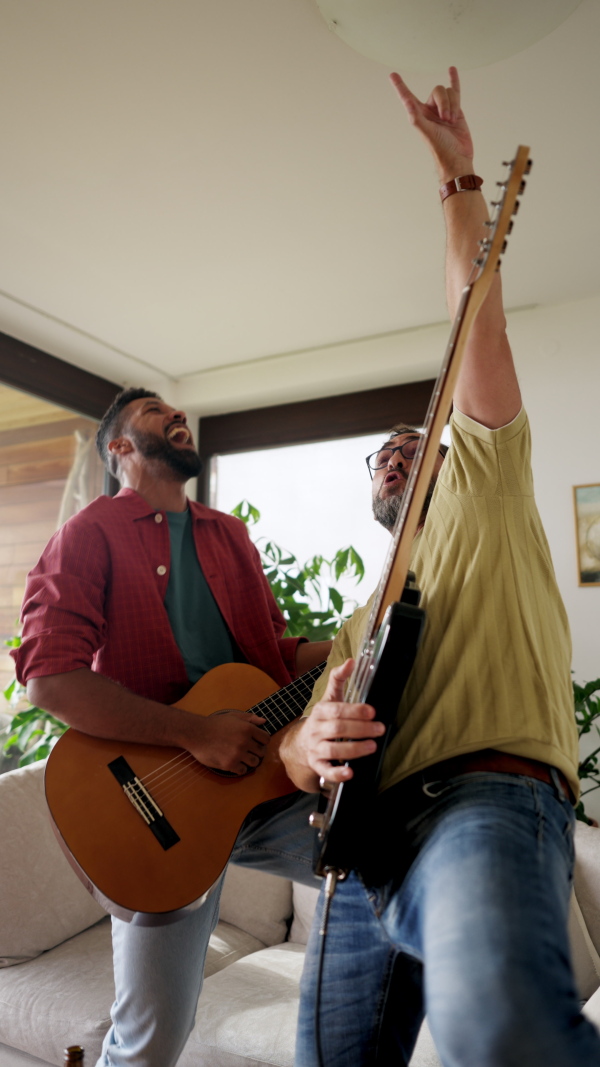 Best friends, musician jamming together. Playing music on acoustic and electric guitar together, having beer and fun. Concept of male friendship, bromance.