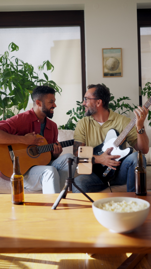 Best friends, musician jamming together. Playing music on acoustic and electric guitar together, having beer and fun. Concept of male friendship, bromance.