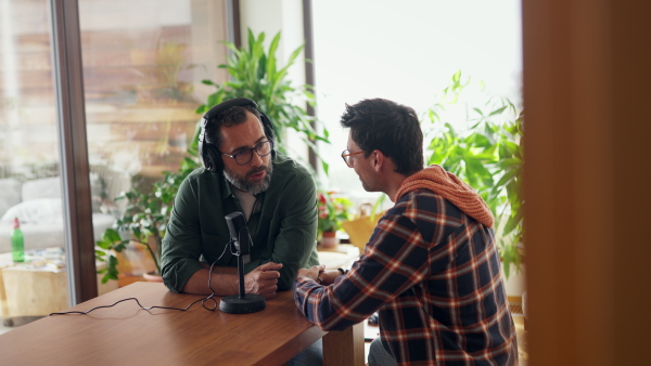 Male friends doing video podcast, talking about difficult topics, sharing sad, hurtful stories. Influencers making live video for social media, creating online content at home.