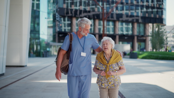 A male caregiver with elderly patient on shopping trip. Geriatric nurse accompany lovely elderly woman on outdoor walk, enjoying conversation.