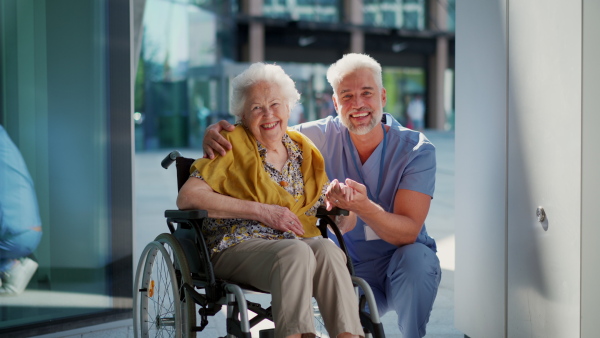 Video of male caregiver with elderly patient on wheelchair. Geriatric nurse taking senior in wheelchair on stroll in the city.