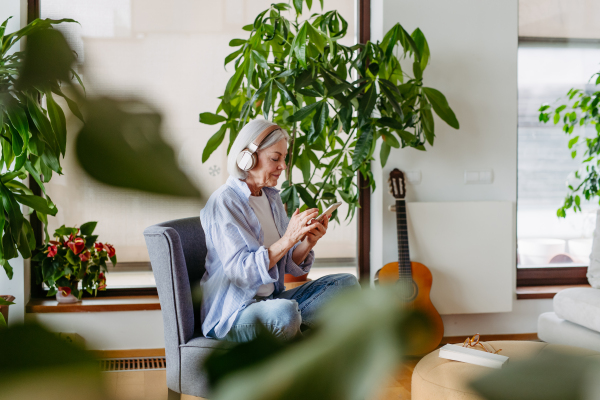 Older woman with headphones on head, listening music, relaxing at home. Concept of weekend activities for mature woman.