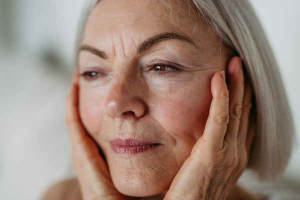 Portrait of beautiful mature woman with gray hair and soft smile, holding her face.