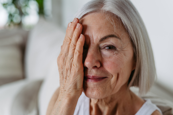 Portrait of beautiful mature woman with gray hair and soft smile, looking at camera. Hand in front of face.