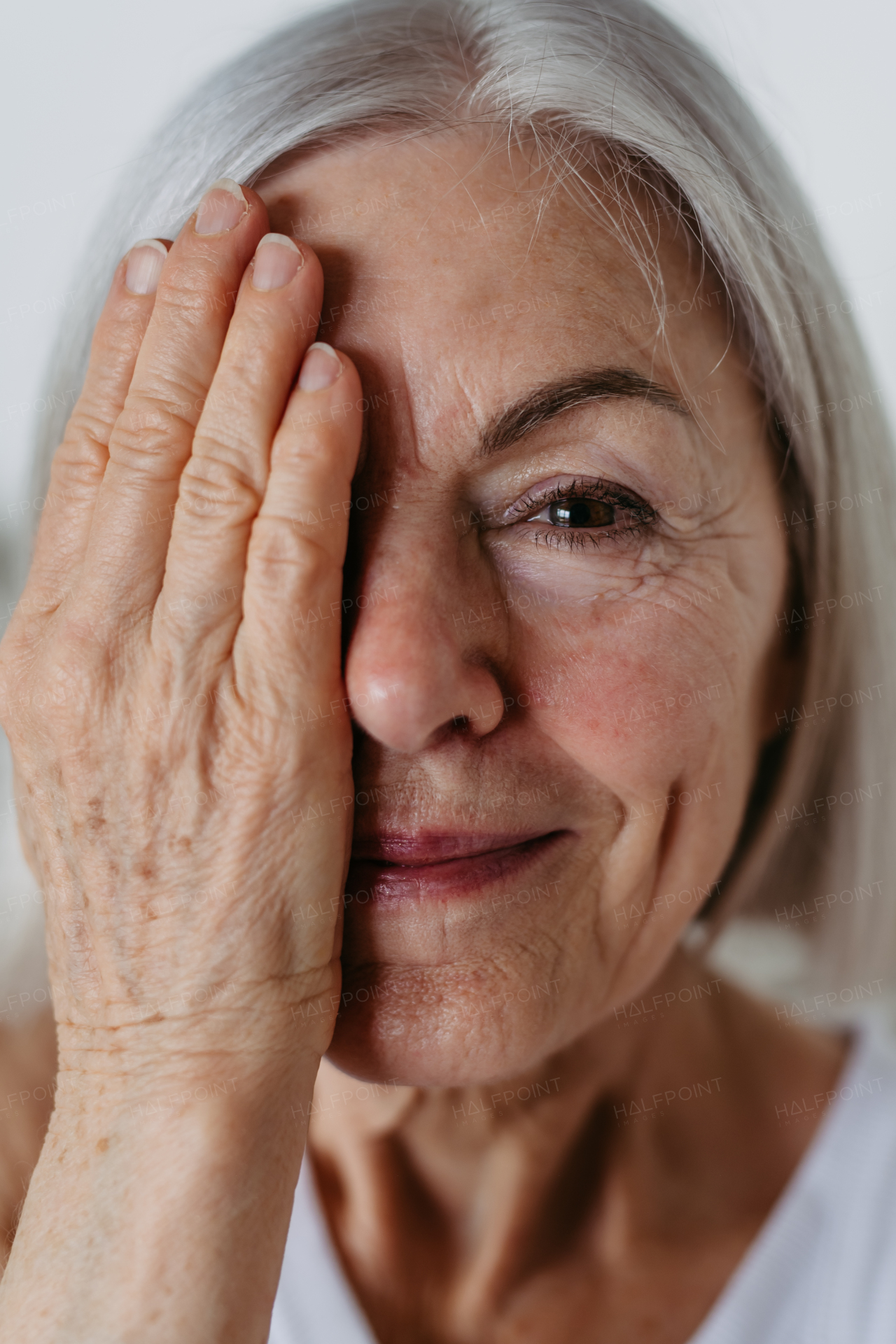 Portrait of beautiful mature woman with gray hair and soft smile, looking at camera. Hand in front of face.