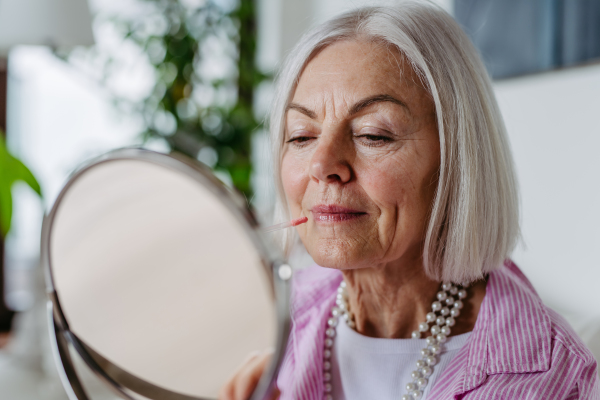 Skincare for mature woman. Portrait of beautiful older woman with gray hair putting makeup on